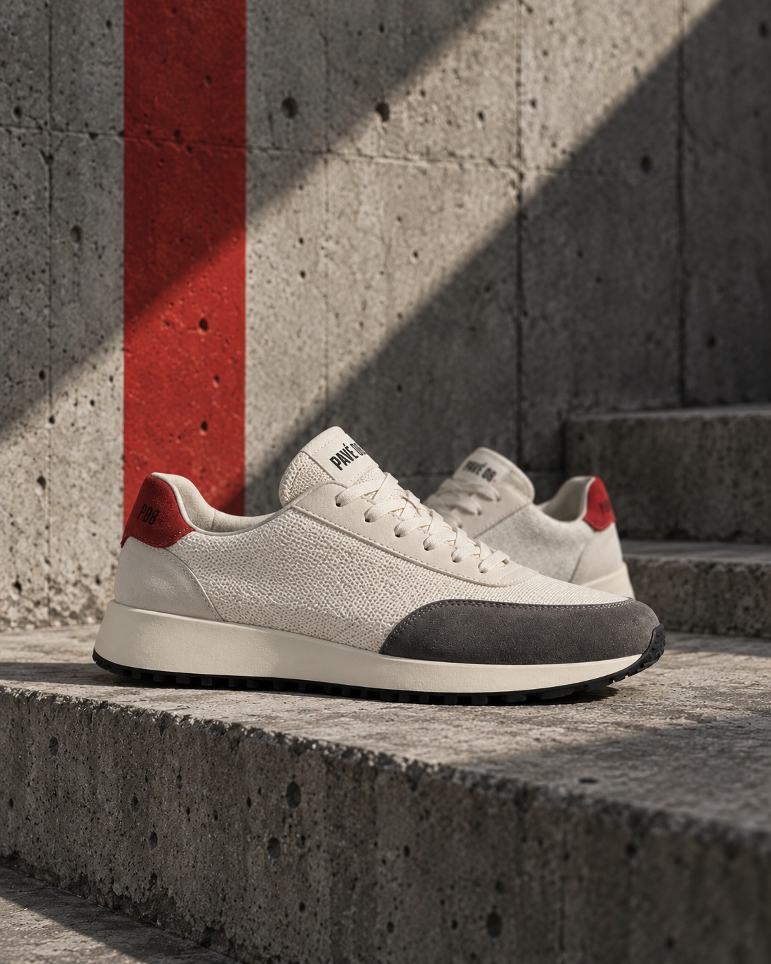 Sneakers ivoire PAVÉ 08 sur un escalier en béton marqué d’une bande rouge.